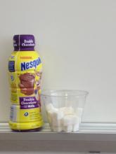 Bottle of Nesquik chocolate milk next to a glass of sugar cubes.
